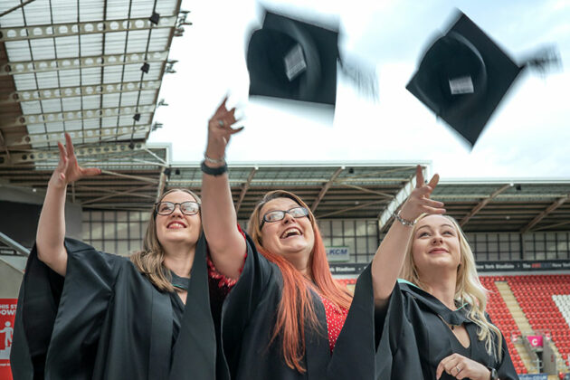 three female graduates throwing their mortarboards into the air