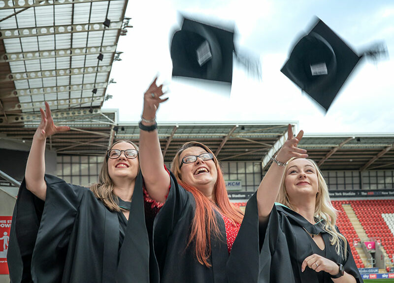 three female graduates throwing their mortarboards into the air