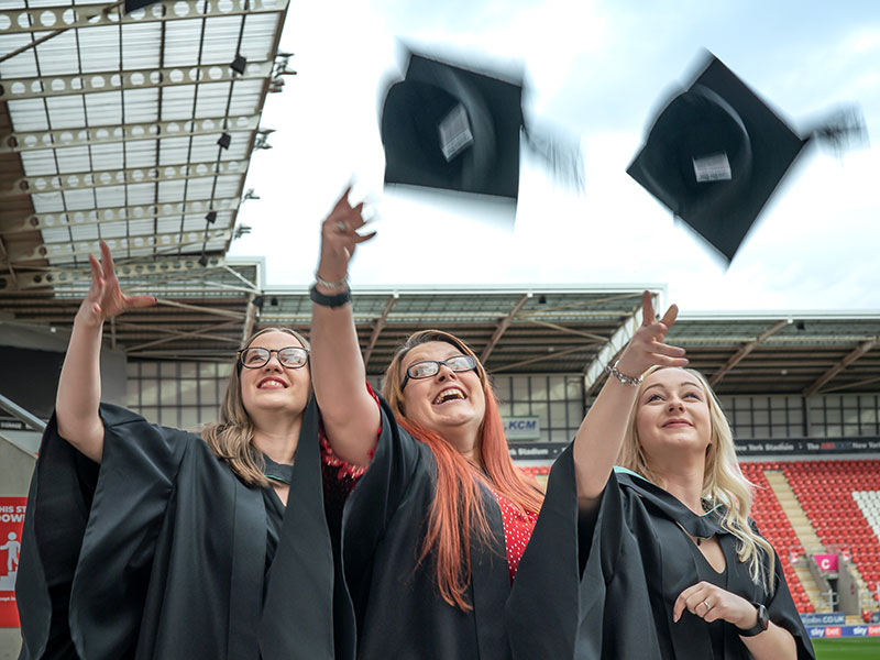 three female graduates throwing their mortarboards into the air