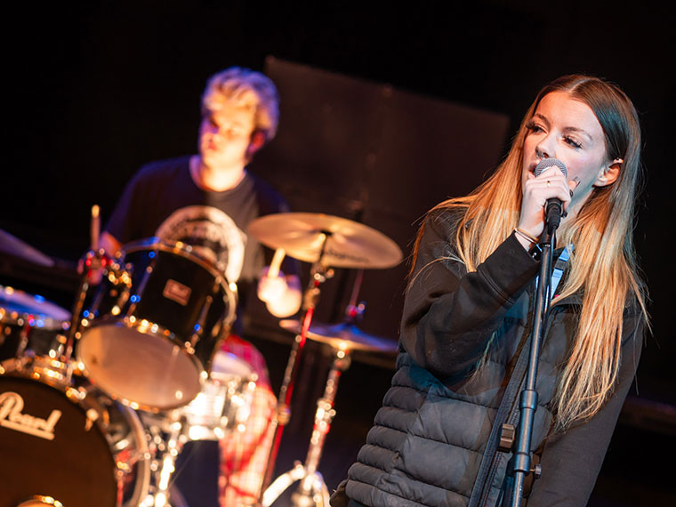 Performing arts student singing and a student on the drums