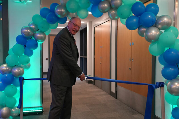 A man cutting a ribbon under a balloon arch