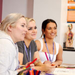 Three smiling students sat in a line at a desk