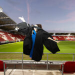 A graduate jumping off the ground throwing their hat in the air