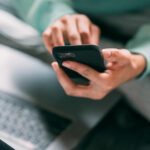 Someone holding a mobile phone next to an open laptop