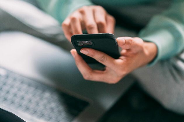 Someone holding a mobile phone next to an open laptop