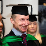 A head and shoulders shot of a smiliing student in graduation attire