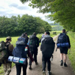 A group of people holding backpacks walking down a path with trees either side